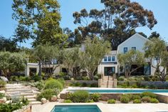 an outdoor swimming pool surrounded by greenery and trees in front of a white house