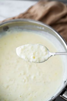 a spoon full of cream sitting on top of a pot filled with milk and cheese