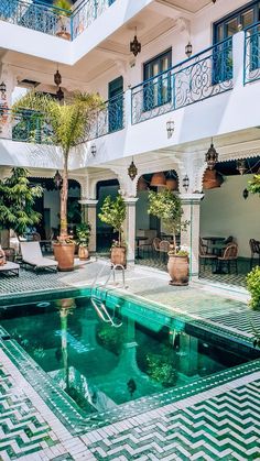 an indoor swimming pool surrounded by potted plants and greenery in front of a white building