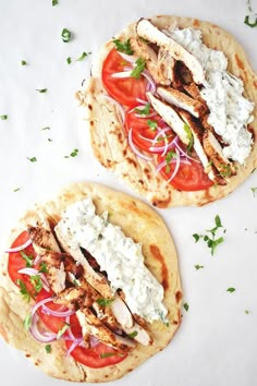 two pita breads topped with chicken, tomatoes and feta cheese on a white surface