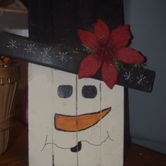 a wooden block with a snowman face painted on it and a poinsetti