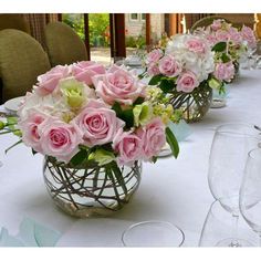 several vases filled with pink and white flowers sit on a table in front of wine glasses