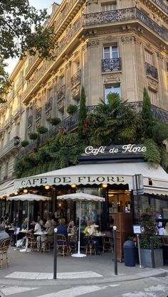 people sitting at tables in front of a building with plants growing on the side of it