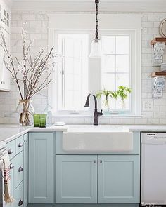 a kitchen with blue cabinets and white walls is pictured in this image, there are flowers on the window sill