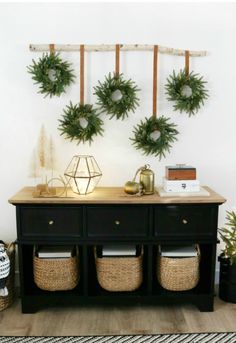 two wreaths are hanging on the wall above a black dresser with baskets underneath it