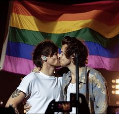 two young men kissing each other in front of a rainbow - colored flag and microphone