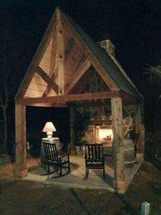 an outdoor fireplace is lit up in the night with rocking chairs and table on the patio