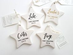 four white ceramic star ornaments with names and date printed on the side, hanging from string