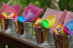 three buckets filled with play doh on top of a wooden table next to trees