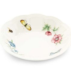 a white plate with flowers and a butterfly on the rim, in front of a white background