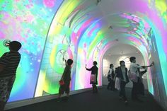 several people are standing in front of an art exhibit with colorful lights on the walls