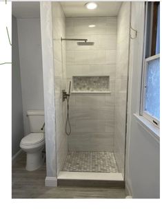 a walk in shower sitting inside of a bathroom next to a white toilet and window