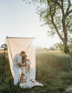 a man and woman are sitting on a stool in front of a white curtain with the sun behind them