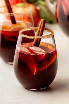 two glasses filled with red liquid and cinnamon stick garnished with apple cider