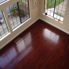 an empty room with wood flooring and three windows looking out onto the yard outside