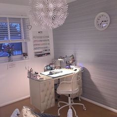 a white desk sitting under a window next to a wall mounted clock and light fixture