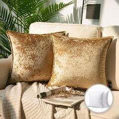 two gold pillows sitting on top of a white couch next to a green palm tree