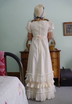 Regency era romantic styled cotton gown with high waist and intricate detail! Ultra-feminine look with short puffed sleeves gathered to cotton bands. The long cotton attached skirt to the fitted bodice has rows of lace, ribbon and cotton ruching at the hem. Skirt is slightly gathered to the fitted bodice. Back zipper closure. Cotton fabric so you can hand wash gently with cold water, lay flat to dry. Designed and made proudly by Recollections in America! Liesa is wearing a petticoat, bonnet,jewe Regency Victorian Dress With Ruffles In Cream, Regency Style Victorian Dress For Vintage Events, Victorian Dress For Garden Party, Regency Style Cream Dress With Ruffles, Vintage Empire Waist Dress With Ruffles For Garden Party, Daywear Prairie Dress With Ruffled Fitted Bodice, Victorian Ruffled Empire Waist Fitted Dress, Fitted Victorian Dress With Empire Waist And Ruffles, Fitted Victorian Dress With Ruffles And Empire Waist