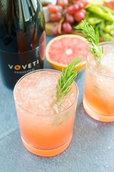 two glasses filled with grapefruit and rosemary garnish next to a bottle of wine