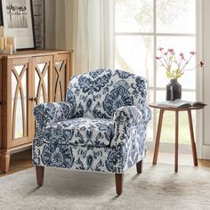 a blue and white chair sitting in front of a window next to a vase with flowers