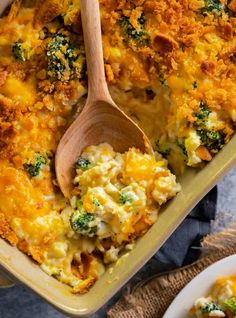 a casserole dish with broccoli and cheese in it, next to a wooden spoon