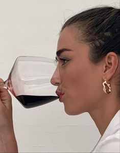 a woman drinking from a wine glass with red wine in her mouth and wearing gold earrings