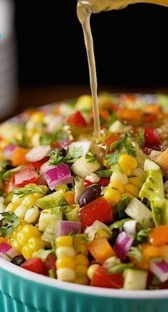 a person pouring dressing into a bowl filled with vegetables and corn on the cob