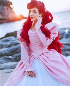 a woman in a pink and white dress is sitting on the rocks by the water