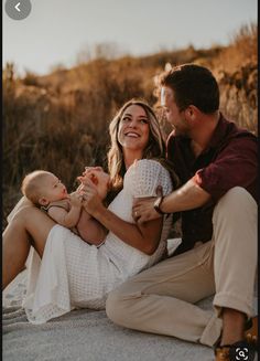 a man and woman holding a baby while sitting on the ground with their arms around each other