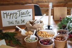 a table topped with cups filled with different types of food next to a sign that says happy trails trail mix bar