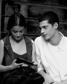 a young man and woman sitting next to each other looking at a cell phone together