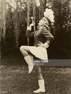 a woman in an old fashioned dress and hat is dancing on the grass with her legs crossed