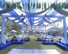 a group of people sitting on blue couches under an open air pavilion with white tables and chairs