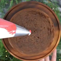 a close up of a person holding a paintbrush in a brown bowl with green plants behind it