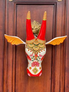 a red and white cow head hanging on a wooden door with gold trimmings