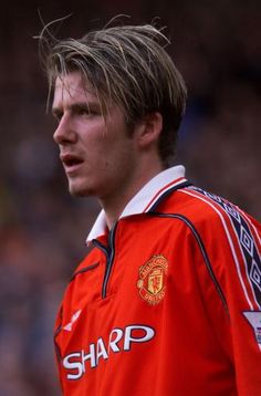 a man in an orange shirt standing on a soccer field with his head turned to the side