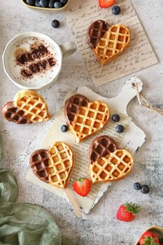 three heart shaped waffles with chocolate on top and strawberries in the background