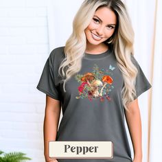 Introducing our Boho Mushroom Botanical Shirt, a charming blend of nature-inspired elements that captures the essence of the great outdoors. This vintage-style tee features whimsical designs of mushrooms, ferns, butterflies, berries, and acorns beautifully arranged to create a delightful autumnal aesthetic. Available in a palette of Ivory, Blue Spruce, Butter, Granite, and Pepper, this shirt not only showcases your love for all things botanical but also easily complements your wardrobe. Crafted Cottagecore Short Sleeve T-shirt For Fall, Cotton T-shirt With Mushroom Design For Fall, Spring Mushroom Print Relaxed Fit Top, Casual Summer T-shirt With Mushroom Design, Fall Mushroom Print Graphic Tee, Fall Mushroom Print Graphic T-shirt, Fall Graphic Tee With Mushroom Print, Summer Graphic Tee With Mushroom Design, Casual Mushroom Design T-shirt For Fall