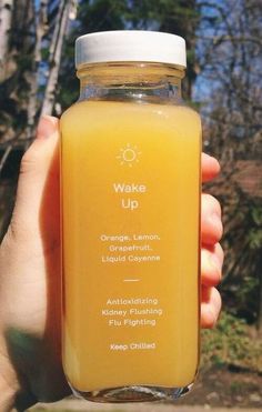 a person holding up a bottle of orange juice with the words wake up on it