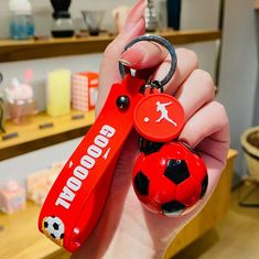 a hand holding a red keychain with a soccer ball on it