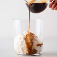 caramel sauce being poured over ice cream in a glass cup on a white surface