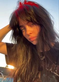 a woman with long hair standing next to the ocean wearing a black shirt and red bow in her hair