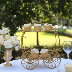 cupcakes are sitting on top of a cart with flowers and wine glasses next to it