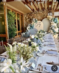 a table set up for an event with flowers and greenery on the tables in front of it