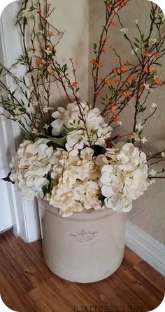 a white bucket with flowers in it on a wooden floor next to a wall and door