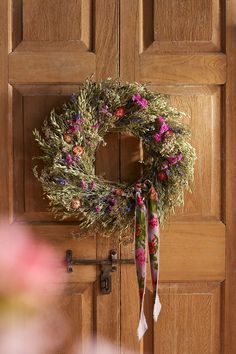 a wreath hanging on the front door of a house with pink and purple flowers around it