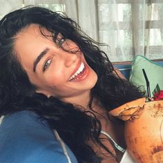 a woman laying on a couch with a large coconut in her hand and smiling at the camera