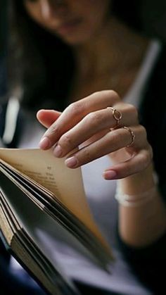 a woman is reading a book with her hand on top of the open book in front of her