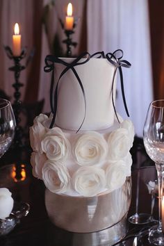 a white wedding cake with roses on top and candles in the background at a reception