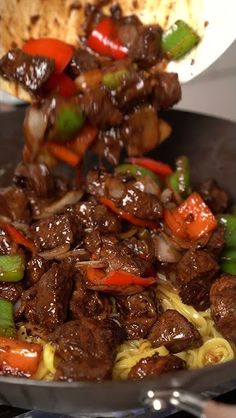 beef and peppers being cooked in a wok on top of the stove with noodles